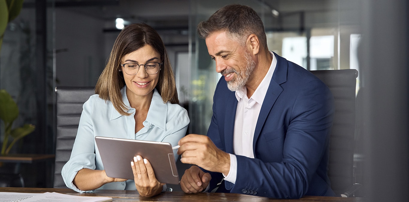Dos trabajadores sénior en una oficina intercambiando opiniones y mirando una tablet
